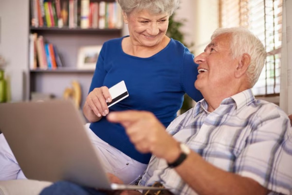 casal de idosos sorrindo com o homem com notebook e mulher com cartaõ do plano saude